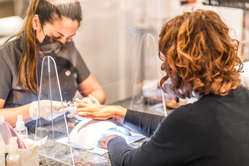 Nail salon worker with face mask and plastic partition